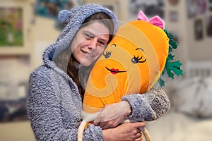 Adult woman in gray terry playsuit with cap with ears hugging a big carrot cuddly toy photo