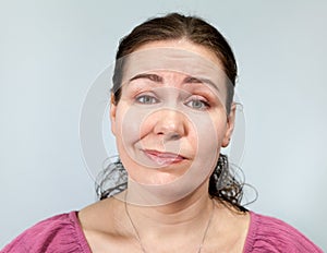 Adult woman with a grin on her face, portrait on grey background, emotions series photo
