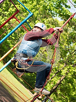 Adult woman in a helmet and with a safety system climbs a rope ladder