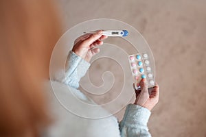 Adult woman holding digital thermometer with high temperature and meds at home close up. Health care lifestyle