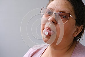 Adult woman holding on tongue a simple white pill, disease treatment concept, taking medication, fulfilling doctor`s prescription