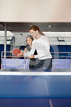 Adult woman instructor teaching male student to play table tennis at sport club