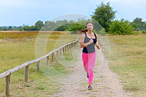 Adult woman jogging towards camera along road
