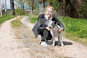 An adult woman in a leather jacket walks her dog on the road.