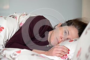 Adult woman lying down in bed suffering from depression looking at camera