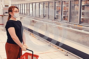 Adult woman in a medical mask stands in a department with frozen foods in a hypermarket. Sale of convenience foods and chilled