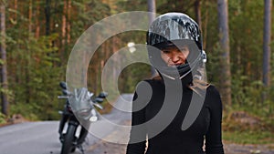 Adult woman motorbike rider fixes her helmet and looking in the camera