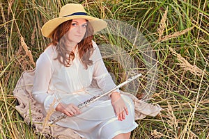 An adult woman with a musical instrument sits on the autumn grass in a field