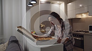 Adult woman opening box, smelling pizza, smiling at domestic kitchen