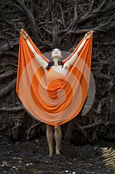 Adult woman in orange dress, dancing under tree roots