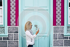 Adult woman outside a coloured house do a phone call with cellular - typical and stylish home - real estate concept for life or