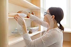 Adult woman picking food from storage cabinet in kitchen, storage with wooden shelves