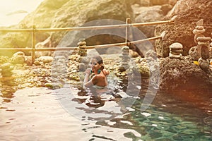 Adult woman posing with a smile in the sun and a thermal spring on the background of rocks
