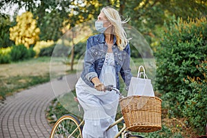 Adult woman in protective mask riding on the retro bike in the green city park