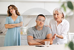 Adult woman quarreling with adult man and elderly women in kitchen