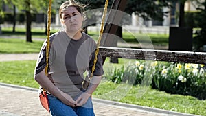 Adult woman riding swing sits with upset expression in park