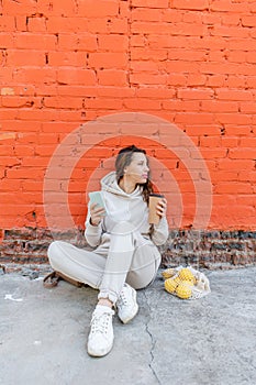 Adult woman sits on the floor with a phone in her hands and a thermo mug with a drink