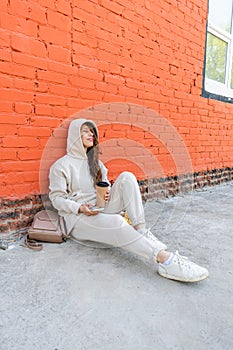 Adult woman sits on the floor with a phone in her hands and a thermo mug with a drink