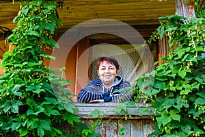 Adult woman sits among greenery on the balcony of a wooden house. Nature.