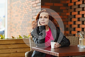 An adult woman is sitting in a summer cafe with a cup of coffee and smiling