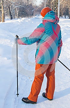 An adult woman in winter sportswear with sticks for Nordic walking poses, standing against the background of the winter landscape
