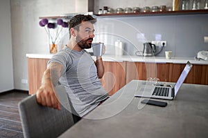 Adult young male with beard drinking coffee  in front of laptop on table. modern lifestyle, relaxed, business concept