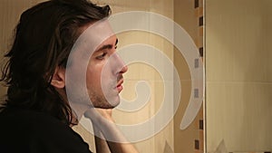 Adult young man brushing long layered dark brown hair in bathroom, standing in front of mirror, face profile