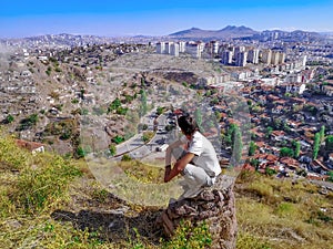 Adult young man squatting on a stone pillar and looking at the Ankara cityscape Turkey - view from the back. A tourist admires