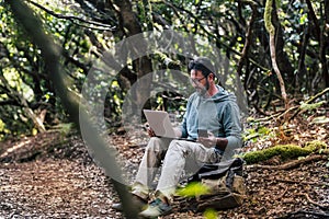 Adult young man work with online roaming connection technology outdoor with phone and laptop computer - people in nature outdoors