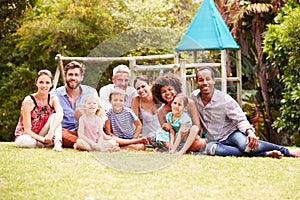 Adults and kids sitting on grass in a garden, group portrait