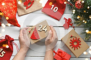 Advent calendar. Merry Christmas. A man`s hands hold a gift box in kraft paper next to other surprises in bags with numbers for