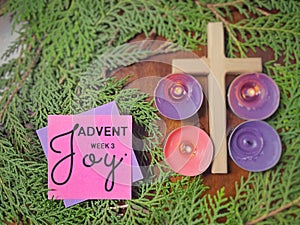 Advent week 3 joy text written on paper with cross, candles and wreath background. Christmas preparation or Advent season concept.