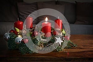 Advent wreath with one burning red candle and Christmas decoration on a wooden table in front of the couch, festive home decor for