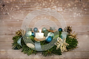 Advent wreath series number one with a lit candle, blue Christmas baubles and decoration on a rustic wooden snowy background,
