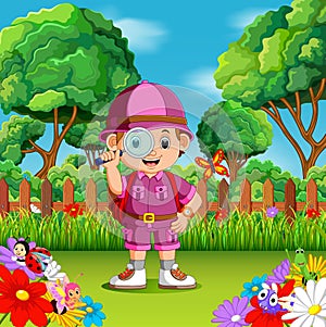 Adventure cute boy holding magnifiying glass in a flower garden