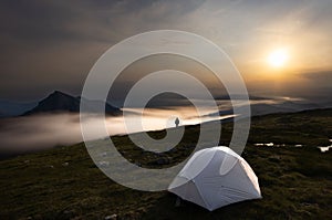 Adventure-seeking outdoorsman in front of a tent on a mysterious foggy mountainous terrain photo