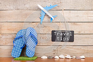 blackboard with text & x22;Travel tips& x22;, plane, seashells on brown wooden background