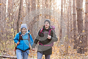 Adventure, travel, tourism, hike and people concept - smiling couple walking with backpacks over autumn natural