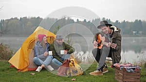 Adventure, travel, tourism and people concept - group of smiling friends with marshmallow sitting around bonfire in