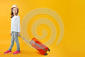Adventure travel trip concept. Happy beautiful cute little girl with an orange suitcase on a yellow background in the studio.
