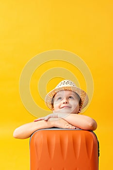 Adventure travel trip concept. Portrait of a cute dreamy little girl with a suitcase. Child close-up on a yellow background.