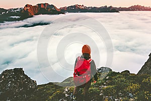 Adventurer backpacker on cliff over clouds in sunset mountains