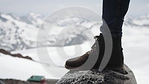 Adventurer feet in leather boot stomps on stone at snowy mountain scenic view