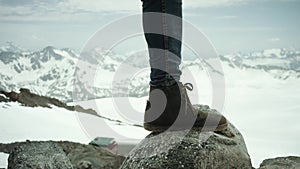 Adventurer feet in leather shoe stomps on rock at snowy mountain scenic view