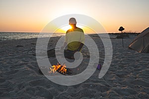 Adventurer sits next to burning bonfire on the beach