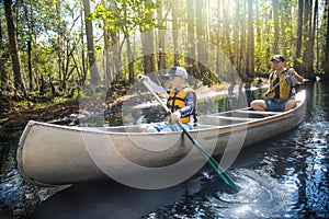 Adventuresome Father and son canoeing together on a beautiful river in a thick forest photo