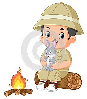 an adventurous boy sits on a fallen tree and holds a rabbit while lighting a bonfire