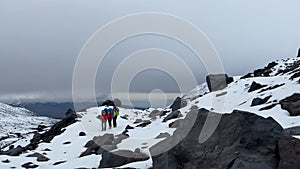 Adventurous climbers with backpacks and trekking poles walk along the snow-covered trail.