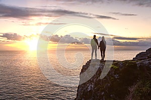 Adventurous couple holding hands and standing on a rocky cliff