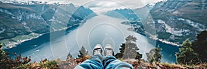 Adventurous hiker s perspective from cliff summit with stunning mountain and lake scenery in view